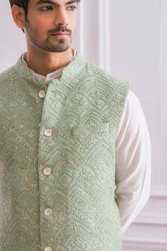 a man wearing a green vest with buttons on the chest and sleeves, standing in front of