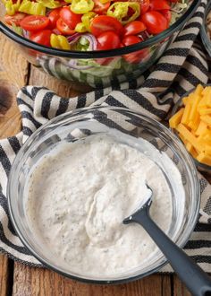 a bowl filled with ranch dressing next to a glass bowl full of cheese and tomatoes