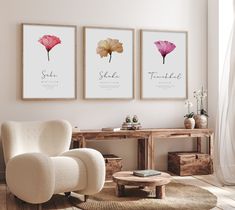 three pink flowers are hanging on the wall above a white chair and coffee table in a living room