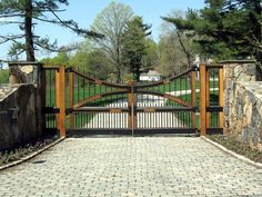 an iron and wood driveway gate with brick pavers walkway leading up to the entrance