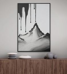 a black and white painting hangs on the wall above a wooden cabinet in a modern living room