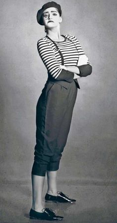 an old fashion photo of a woman with her arms crossed, wearing a hat and striped shirt