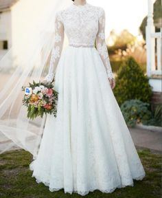 a woman in a white wedding dress standing on the grass with her veil over her head