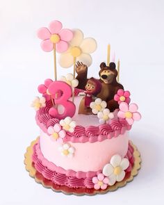 a pink birthday cake with two bears on top and flowers in the middle, sitting on a plate