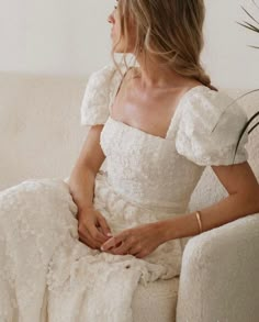 a woman in a white dress sitting on a couch with her hands under her knees