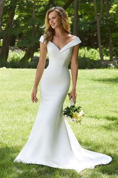 a woman in a white wedding dress walking through the grass with her bouquet on her hand