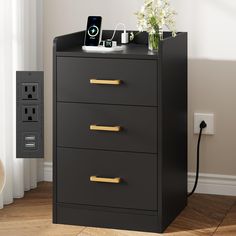 a black and gold filing cabinet with flowers on top, phone charging in the background