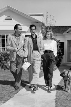 three people and a dog walking in front of a house