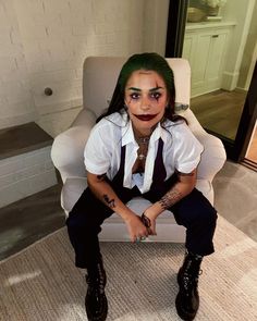 a man with green hair sitting in a chair wearing a clown makeup and tie on