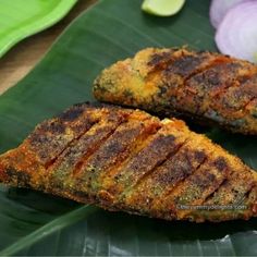 two pieces of meat sitting on top of a banana leaf next to onions and limes