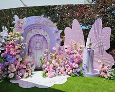 there is a purple fairy door surrounded by pink flowers and other decorations on the grass