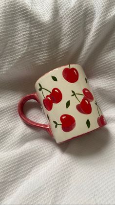 a red and white ceramic cup with cherries on it sitting on a white sheet