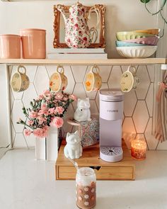 a coffee maker sitting on top of a counter next to pink flowers and other items