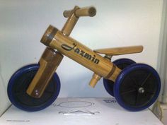 a wooden toy bike sitting on top of a cardboard box next to a white wall