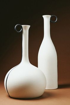 two white vases sitting next to each other on a brown tableclothed surface