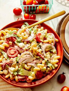 a red bowl filled with pasta salad next to tomatoes and other vegetables on a table