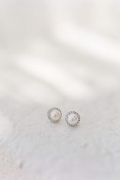 pair of pearl and diamond stud earrings on white fabric background, closeup view from above