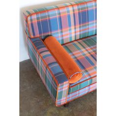 an orange and blue plaid couch sitting on top of a carpeted floor next to a wall