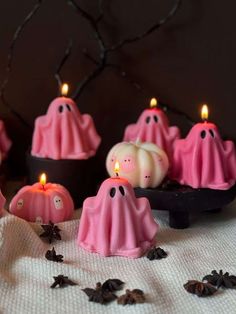 some pink candles with ghost faces on them sitting in front of pumpkins and bats