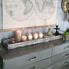 a dresser with candles on it and a map hanging above the drawers in front of it