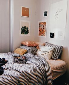 an unmade bed in a small room with pictures hanging on the wall above it