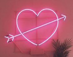 a pink neon heart with an arrow in the middle and a palm tree next to it