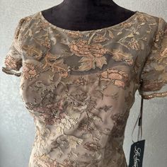 a dress on a mannequin with gold and pink flowers in the back,