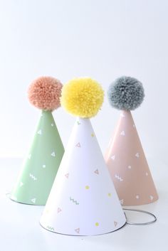 three small party hats with pom - poms on top, one in pastel colors