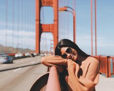 a woman sitting on the side of a road talking on her cell phone while standing next to a bridge