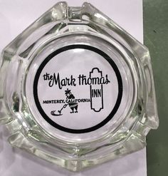 the mark thomas logo on a clear glass ashtray with black and white lettering that reads,'money california inn '