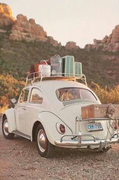 an old vw bug with luggage on the roof is parked in front of some mountains