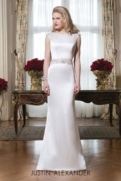 a woman standing in front of a window wearing a white dress with beading on it