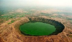 an aerial view of a green lake surrounded by dirt