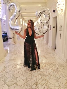 a woman in a black dress is holding two large silver balloons and posing for the camera