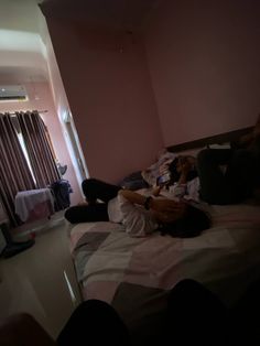 two people laying on a bed in a room with pink walls and curtains, one person is sleeping