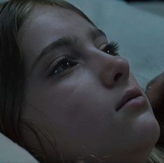 a close up of a person laying in bed with her eyes closed and one eye open