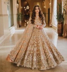 a woman in a gold and white bridal gown posing for the camera with her hands on her hips