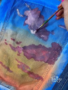 someone is painting clouds on a jean jacket