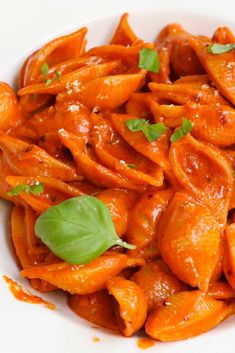 a white bowl filled with pasta covered in sauce and garnished with green leaves