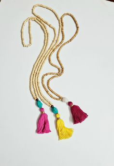 a necklace with beads and tassels on a white surface, next to a pen