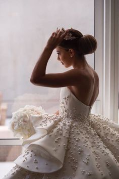 a woman in a wedding dress looking out the window with her hand on her head