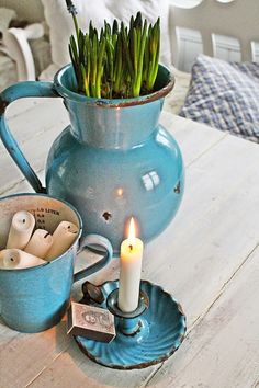 a blue vase filled with green plants sitting on top of a table next to a candle