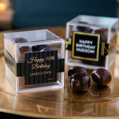 two clear boxes with chocolates in them on a gold tray and one has a happy birthday sign