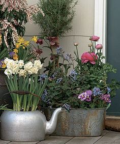 some flowers are in pots on the side of a building and there is a watering can next to them