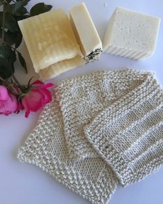 some soaps and flowers are laying on a white counter top next to a knitted sweater