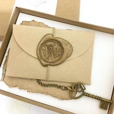 an envelope with a key attached to it and a wax stamp on the front in a box