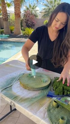 a woman cutting broccoli on top of a table next to a swimming pool