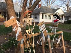 two skeleton statues in front of a house with trees and flowers on the lawn, one is wearing a pirate's hat