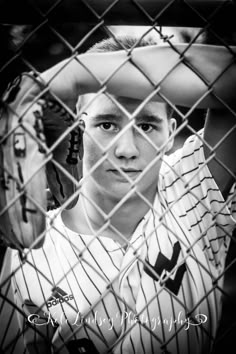 a young man holding a baseball bat behind a chain link fence in black and white