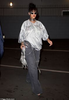 a woman walking across a parking lot wearing sunglasses and a silver top with an animal print purse